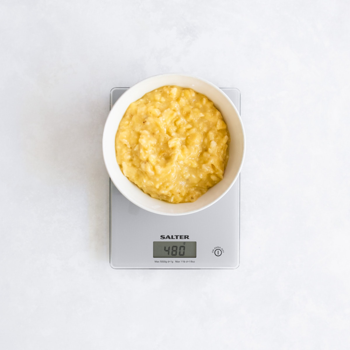 A bowl of mashed banana sitting on a set of digital scales.