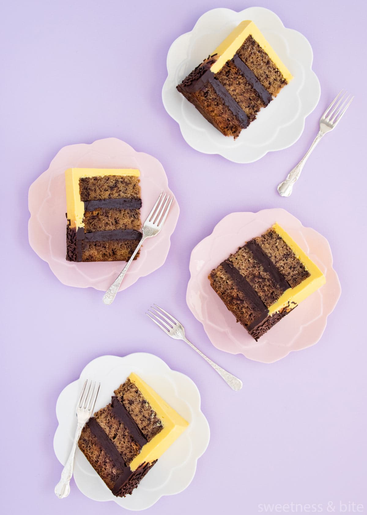 Four slices of banana cake on pink and white plates, on a purple background.