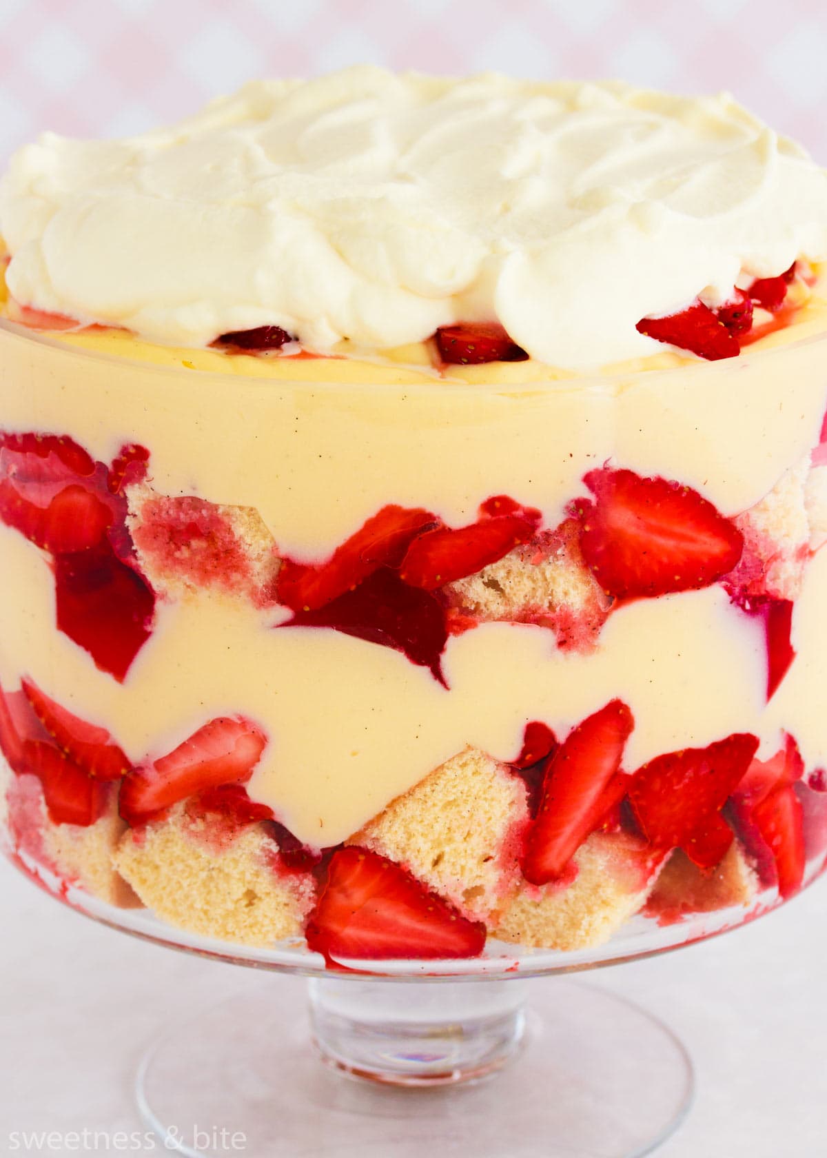 Close up of the layers in the gluten free trifle - sponge cake, strawberries, pink jelly, custard and whipped cream.