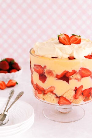 Gluten free trifle in a footed glass bowl on a pink background.