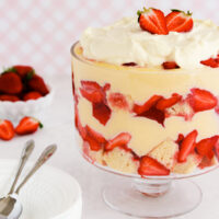 Gluten free trifle in a footed glass bowl on a pink background.