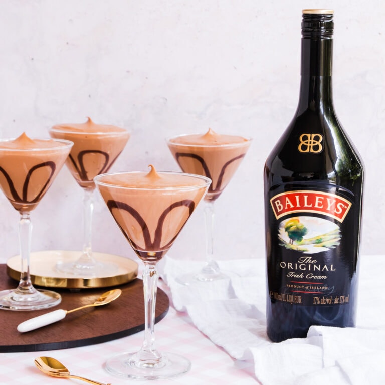 Four cocktail glasses filled with Baileys mousse, with a Baileys bottle in the background.