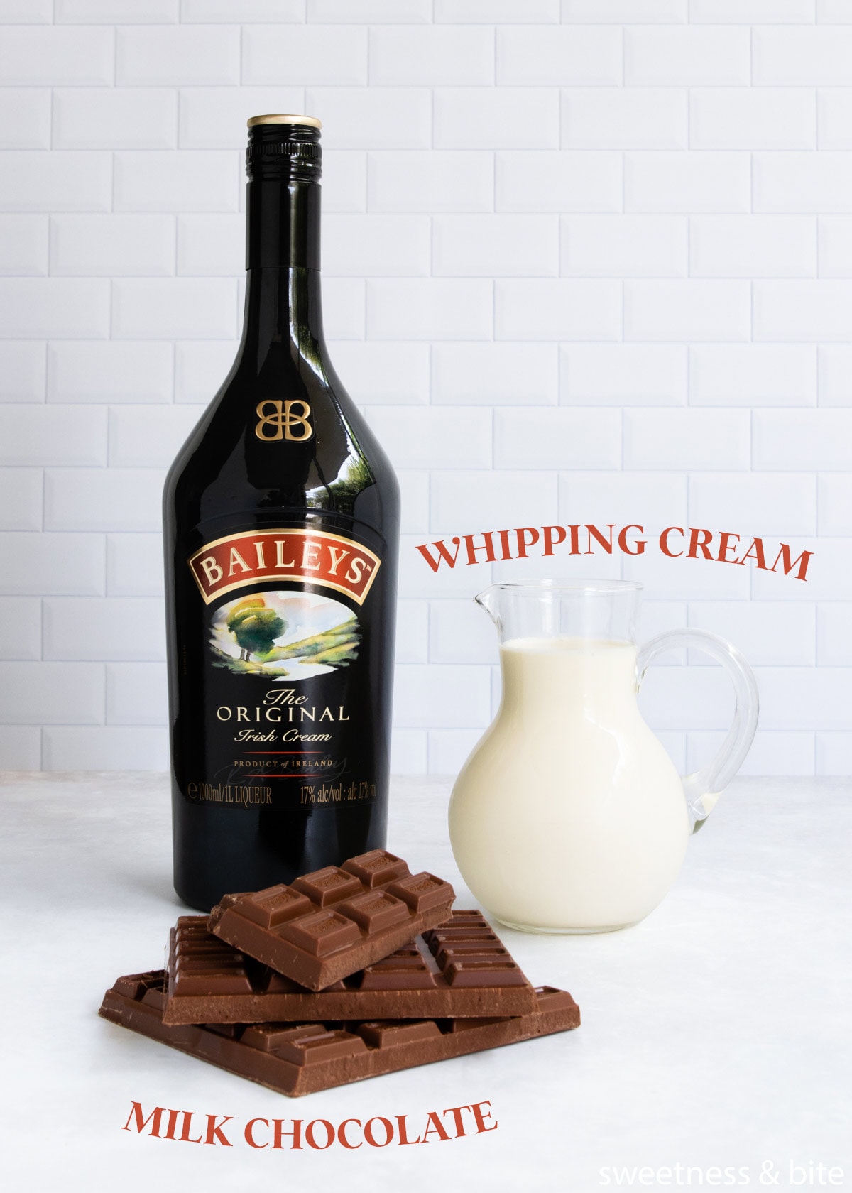 The baileys mousse ingredients - milk chocolate, whipping cream and baileys irish cream, on a white tiled background.