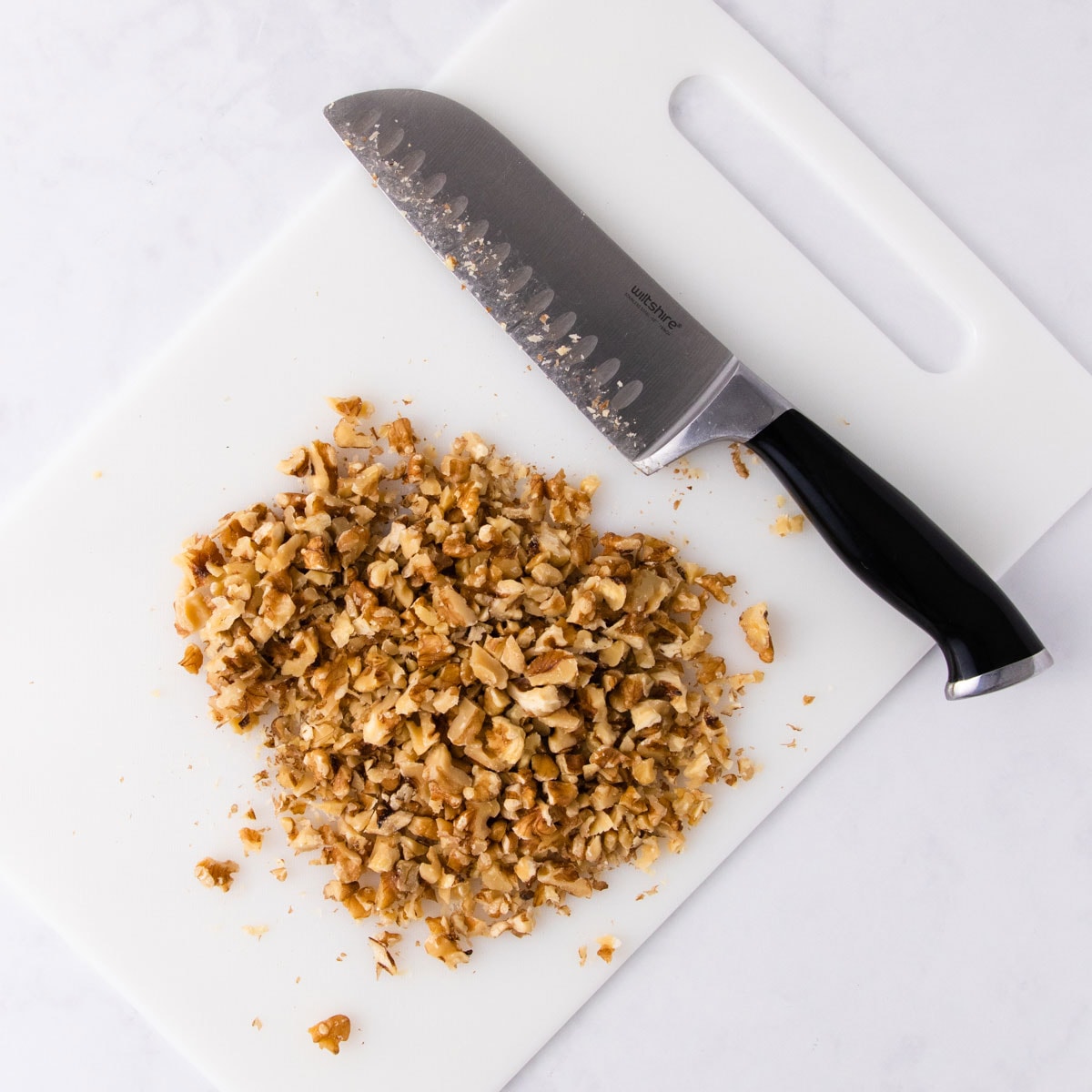 Chopped walnuts on a white chopping board, next to a large chef's knife with a black handle.