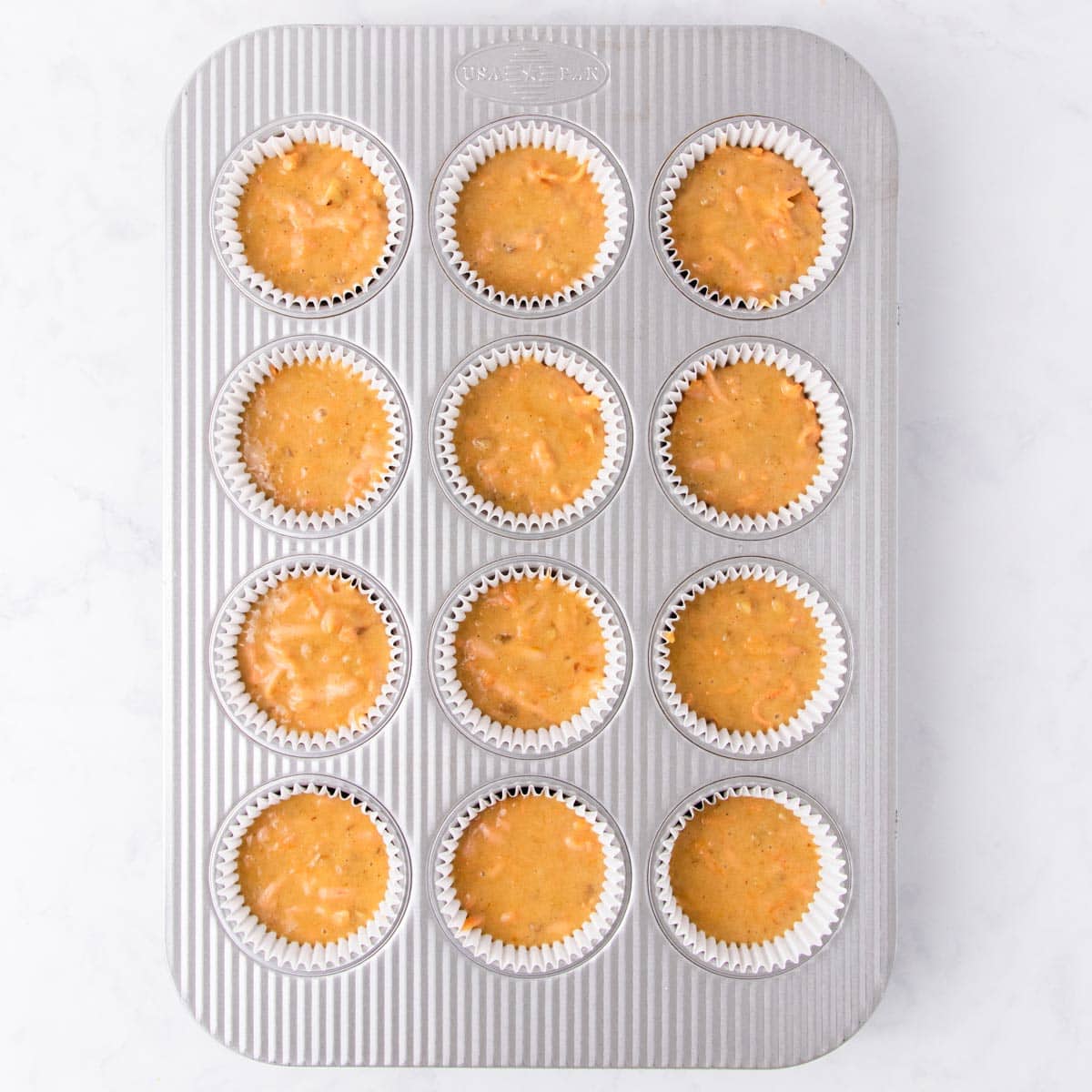 The cupcake batter in a 12-hole muffin pan lined with white cupcake liners.