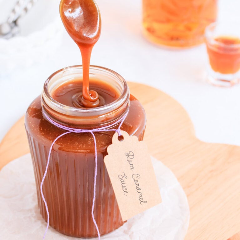 Rum caramel sauce falling from a spoon in a thick ribbon back into a ribbed glass jar.