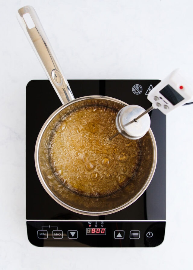 The caramel beginning to turn golden, with a sugar thermometer clipped to the side of the pan.