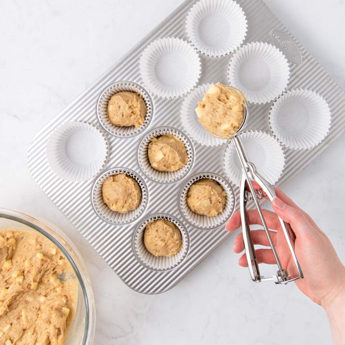 The muffin batter being spooned into the muffin tin using a large cookie scoop.
