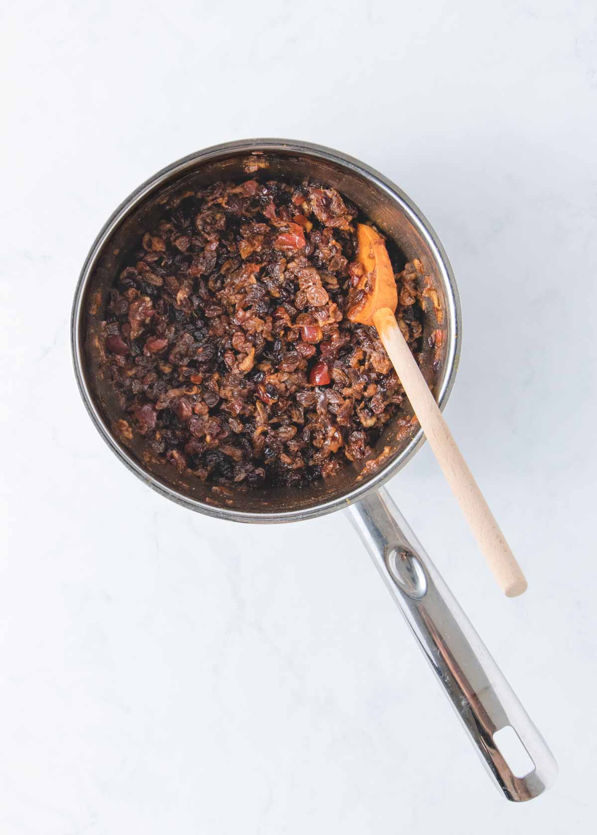 The cooked fruit mince in a pan with a wooden spoon.