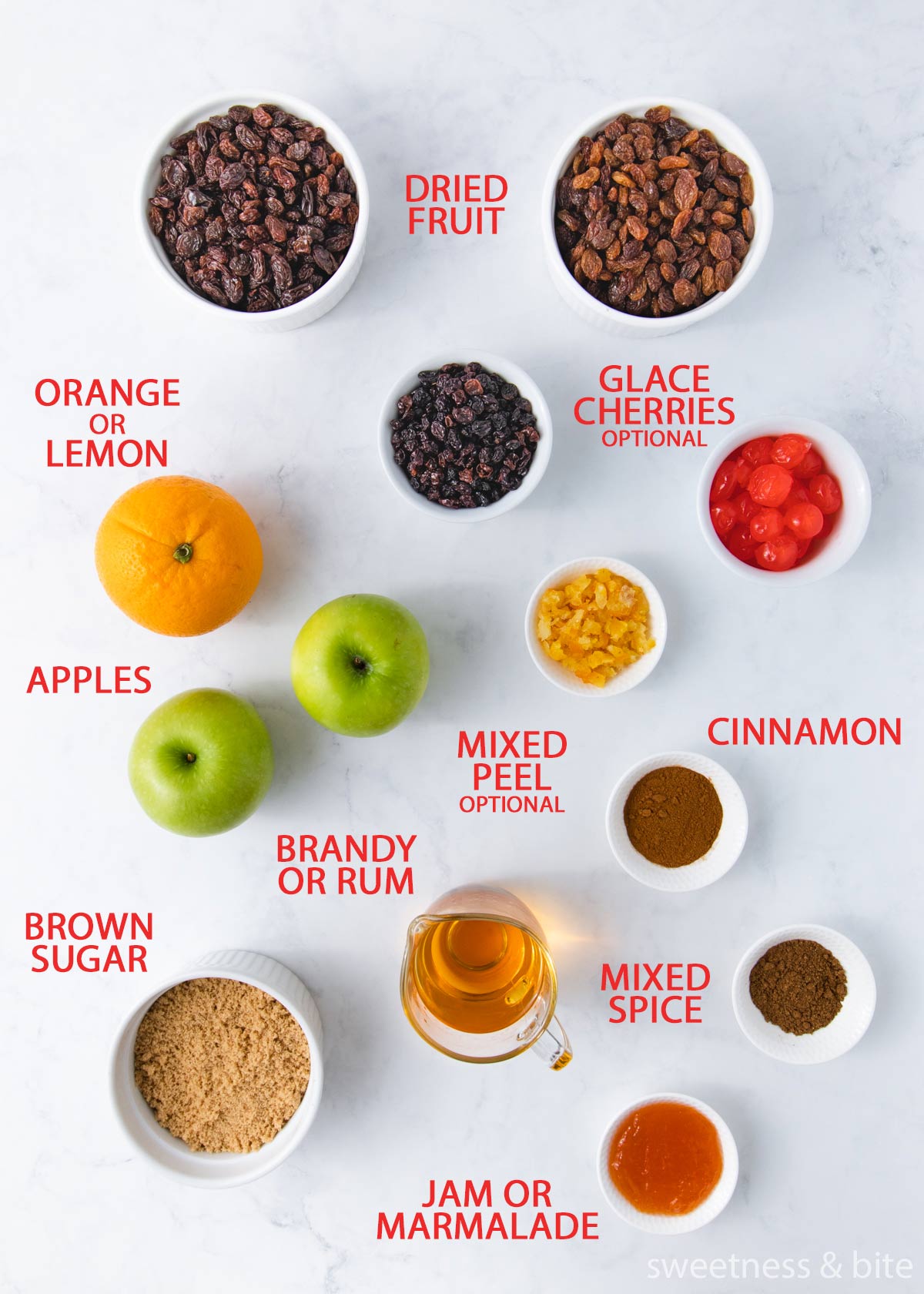 The fruit mince ingredients laid out on a grey marble background with labels - dried fruit, cherries, orange, mixed peel, apples, spices, brown sugar, rum and jam.