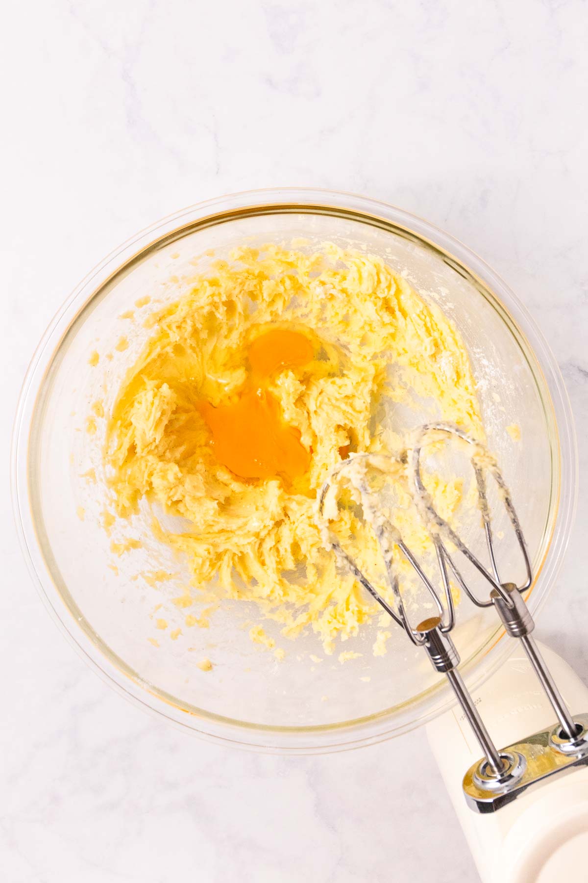 The creamed butter and sugar mixture, with an egg added, in a large glass bowl.
