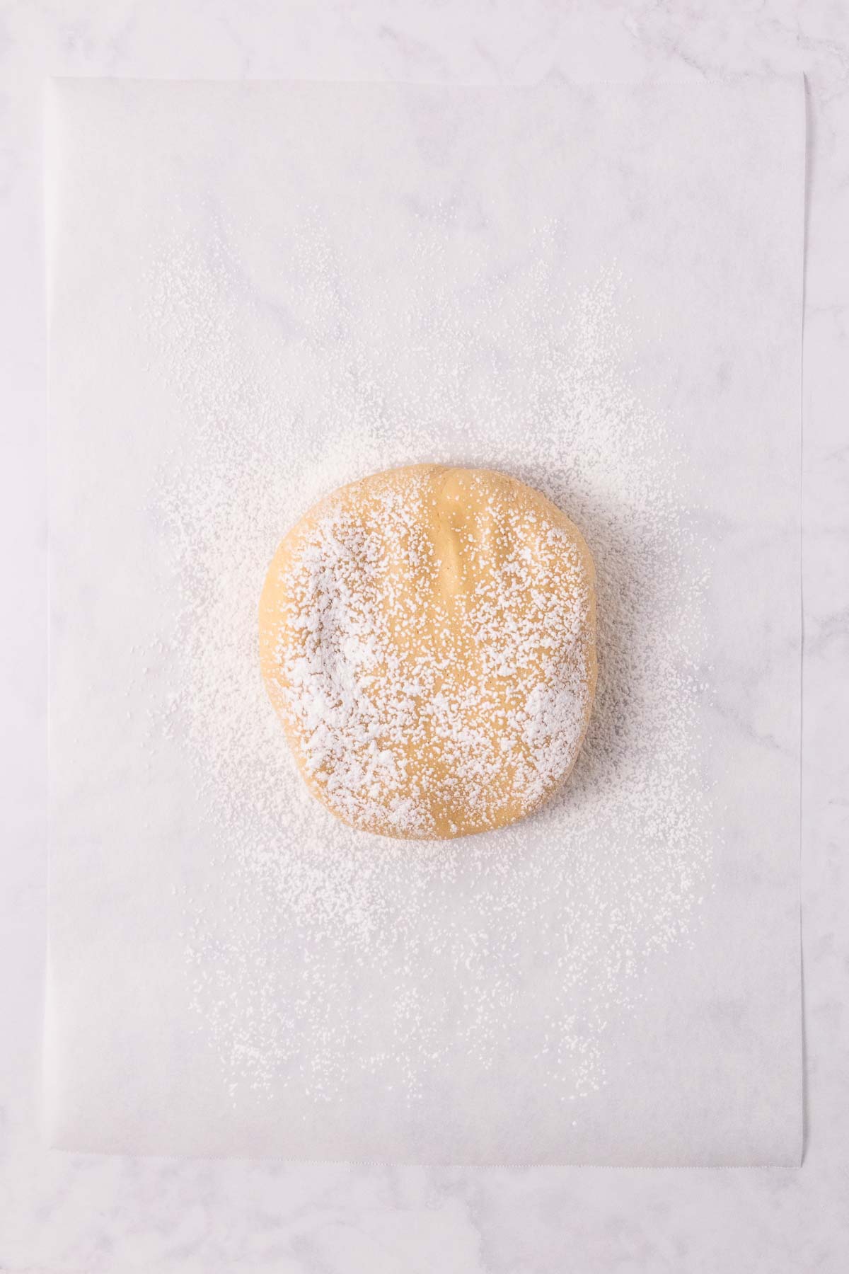 The ball of dough, dusted with flour, on a flour dusted sheet of baking paper.