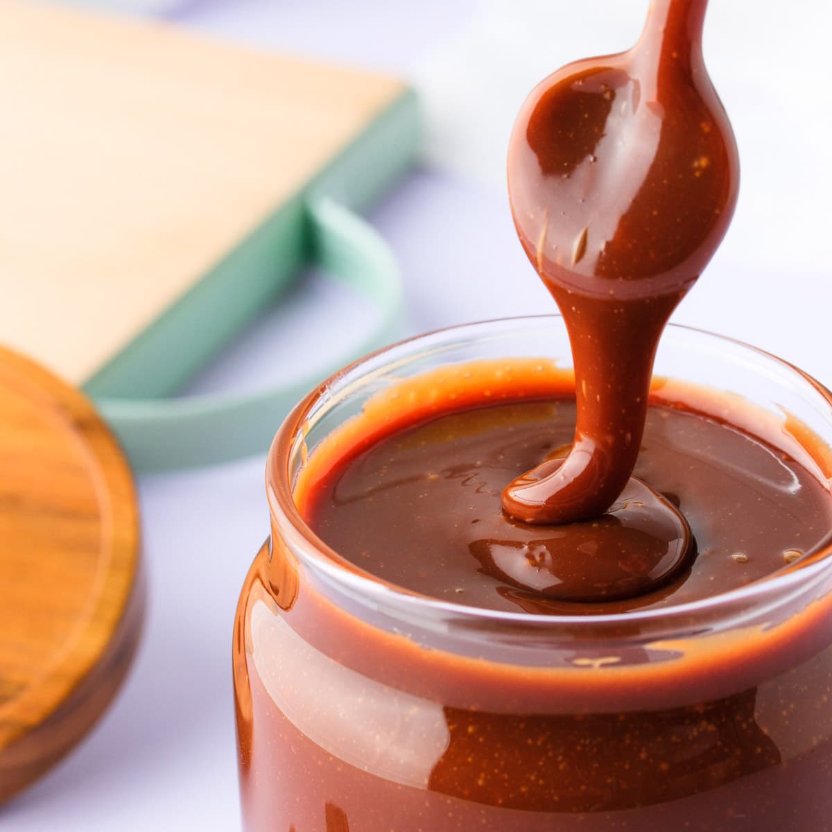 A close up of a jar of chocolate caramel sauce, with a spoon drizzling the thick sauce back into the jar.