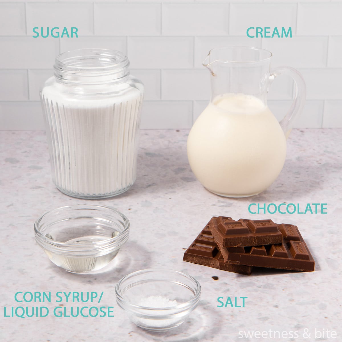 The ingredients for chocolate caramel sauce in glass containers on a grey background - sugar, cream, corn syrup, salt and chocolate.