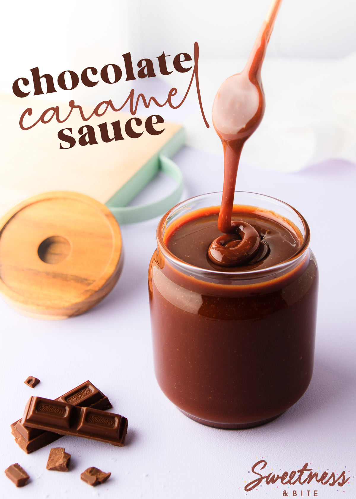 A jar of chocolate caramel sauce on a pale purple background, with a spoon drizzling the thick sauce back into the jar, and some chopped chocolate next to the jar.