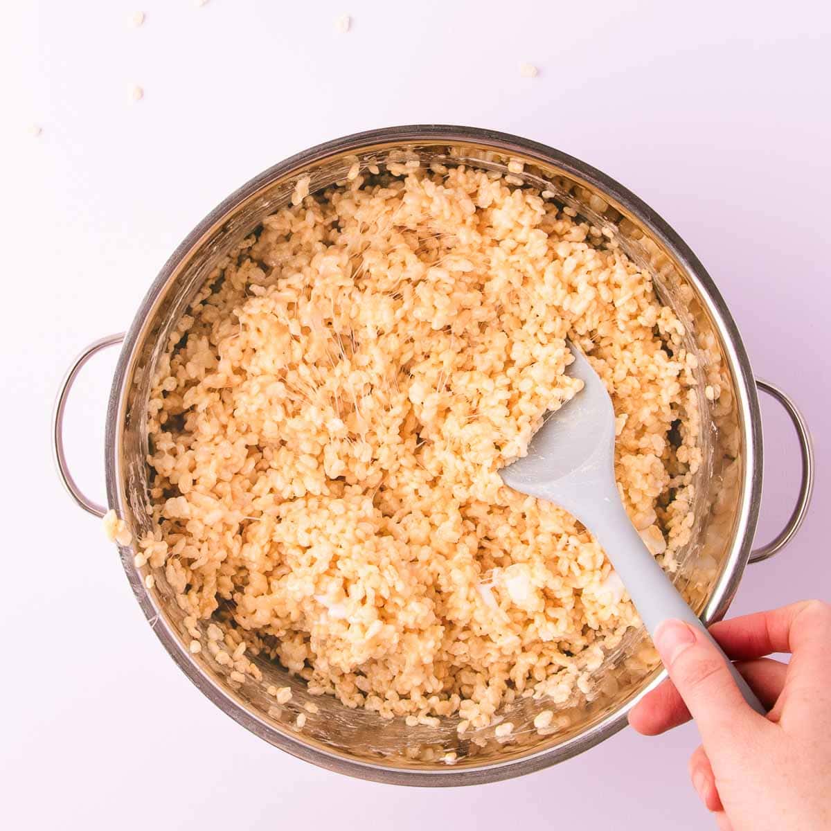 The rice crispy cereal being stirred into the sticky marshmallow mixture.