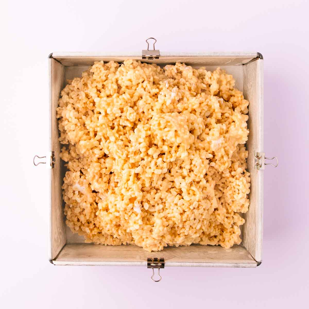 The rice krispie mixture piled into a baking paper lined square cake pan.