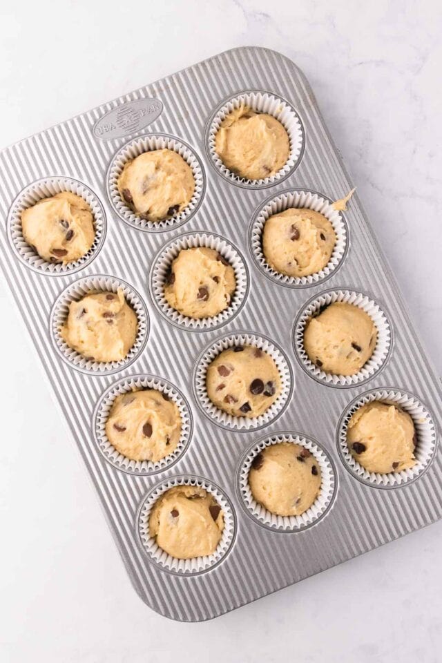 The muffin batter in a 12-hole muffin pan lined with paper muffin cases.
