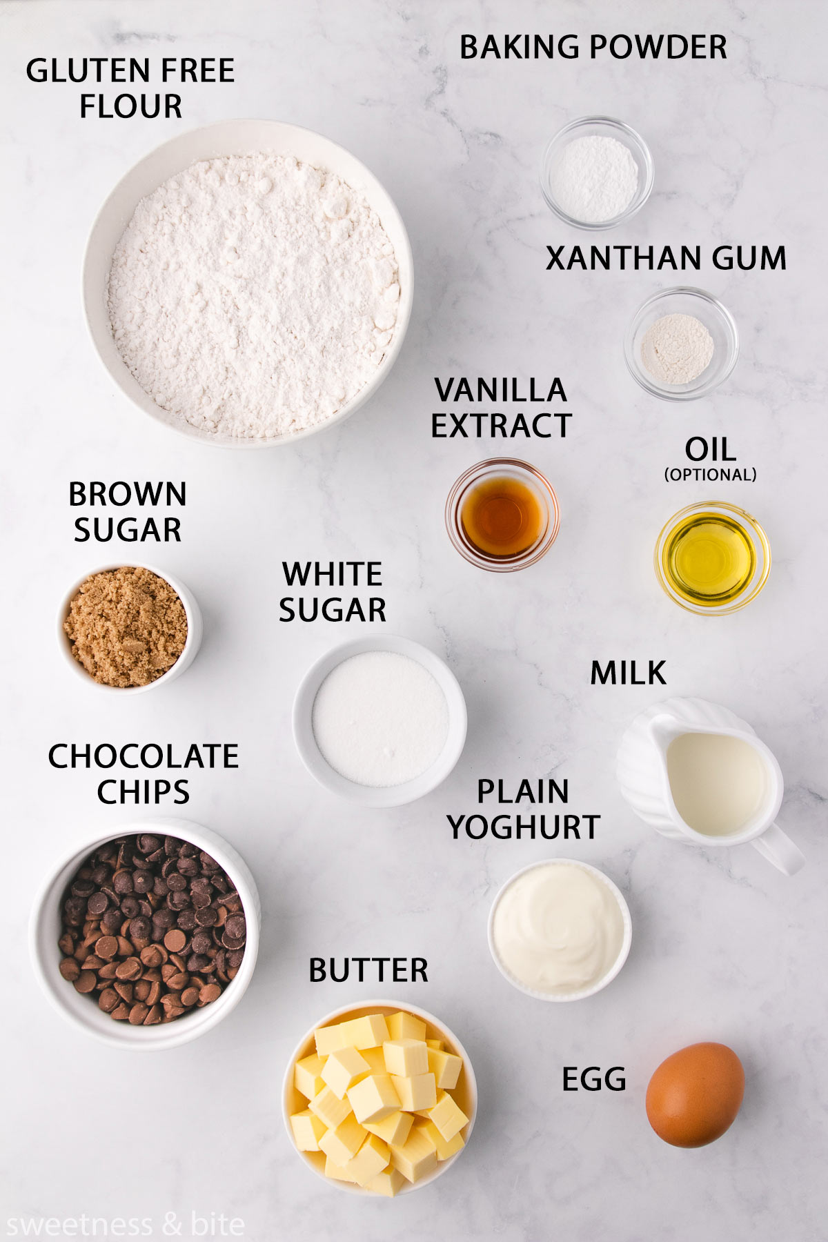 The gluten free chocolate chip muffin ingredients in white bowls on a light grey marble background.