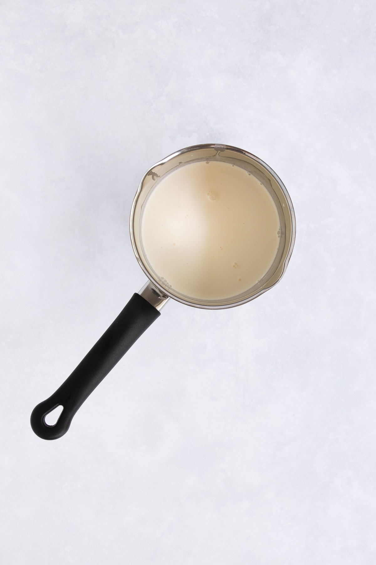 Cream in a small stainless steel saucepan with a black handle. 