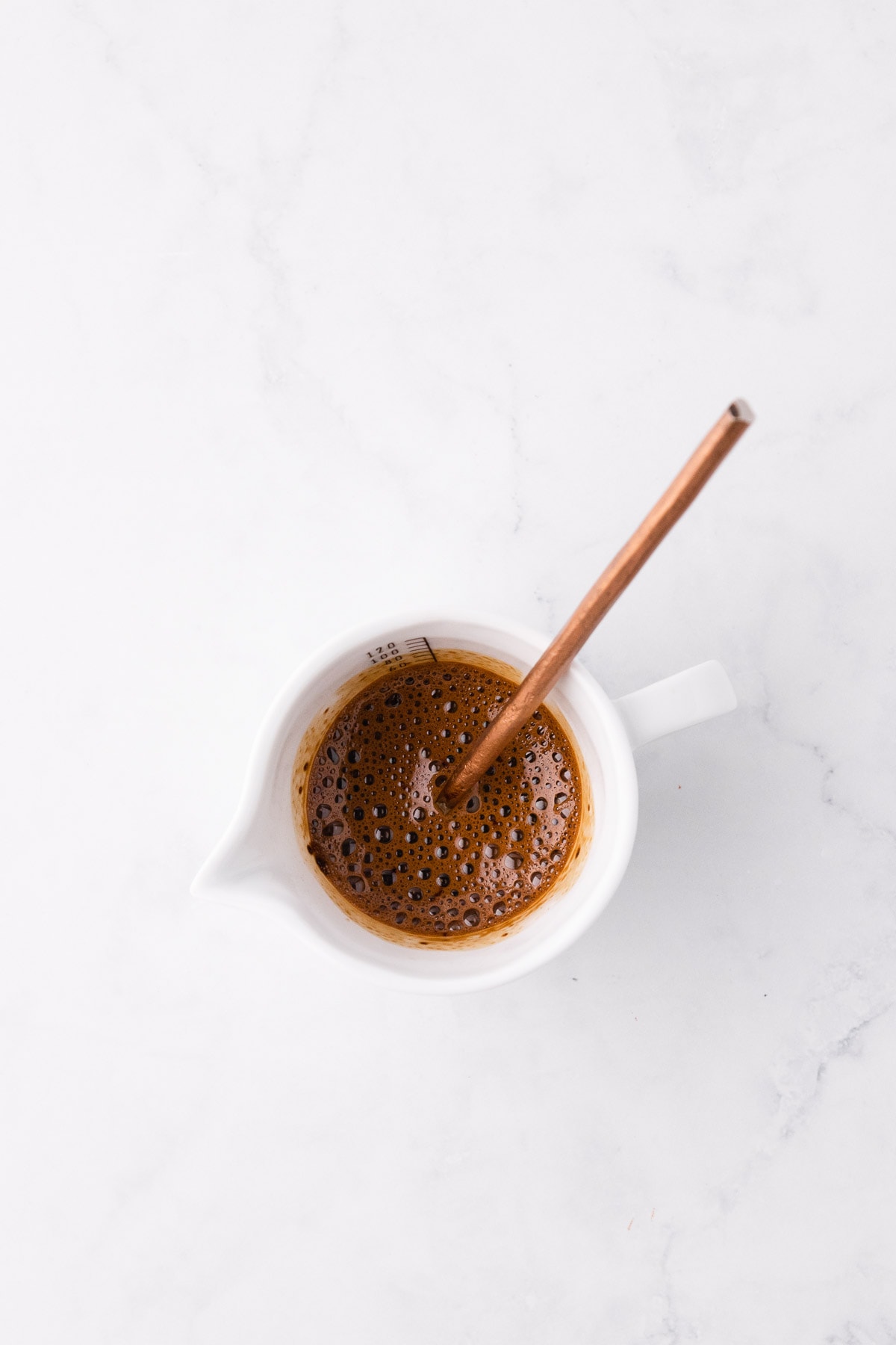 Instant coffee dissolved in water, in a very small white ceramic jug, with a copper handled-spoon.