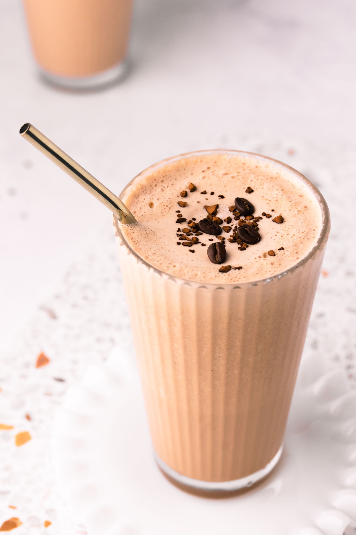 A close up of the top of a coffee milkshake, decorated with a sprinkle of coffee granules and four coffee beans. 