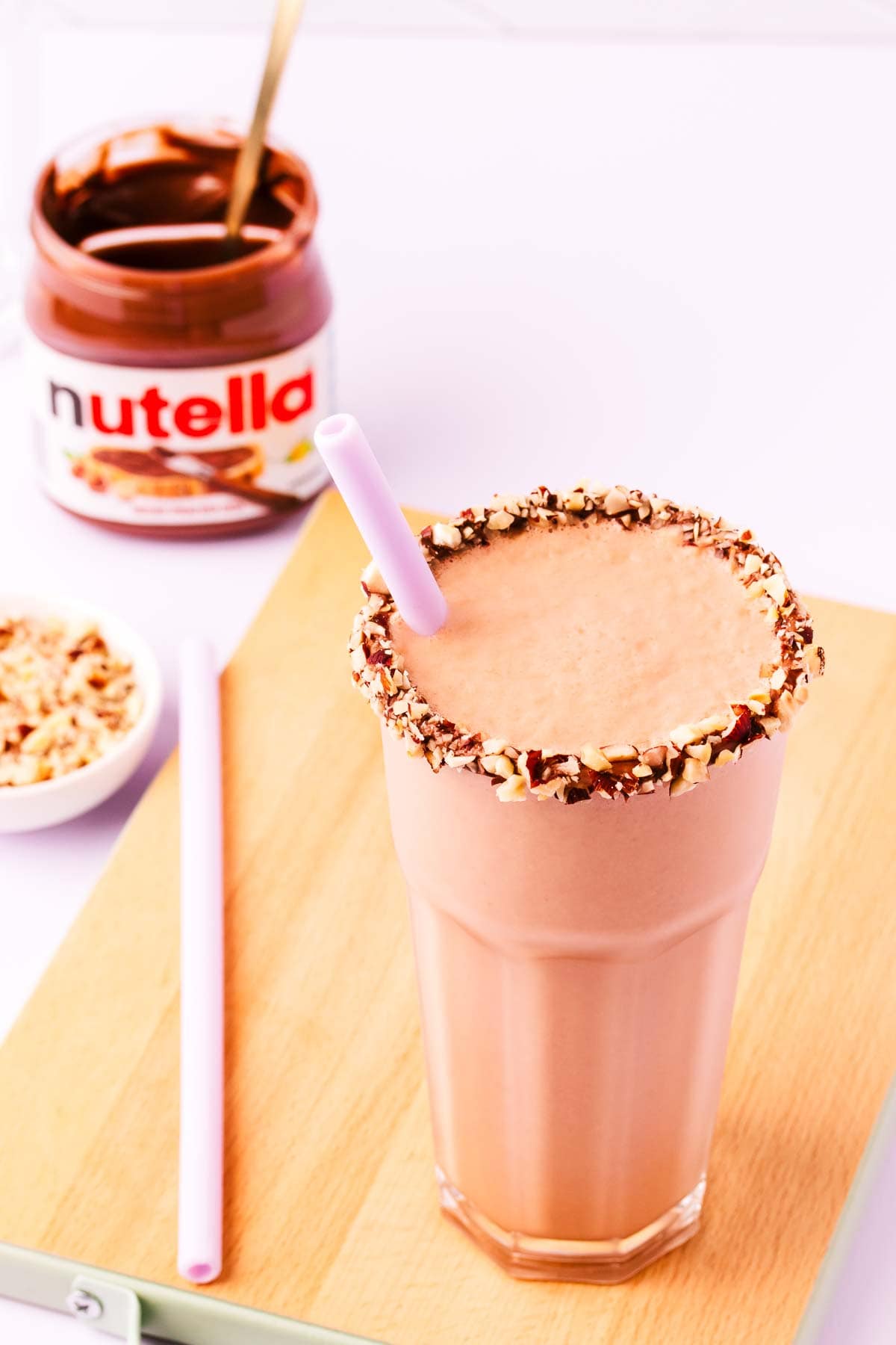 Close up of the top of a Nutella milkshake, with Nutella and hazelnuts around the rim of the glass.