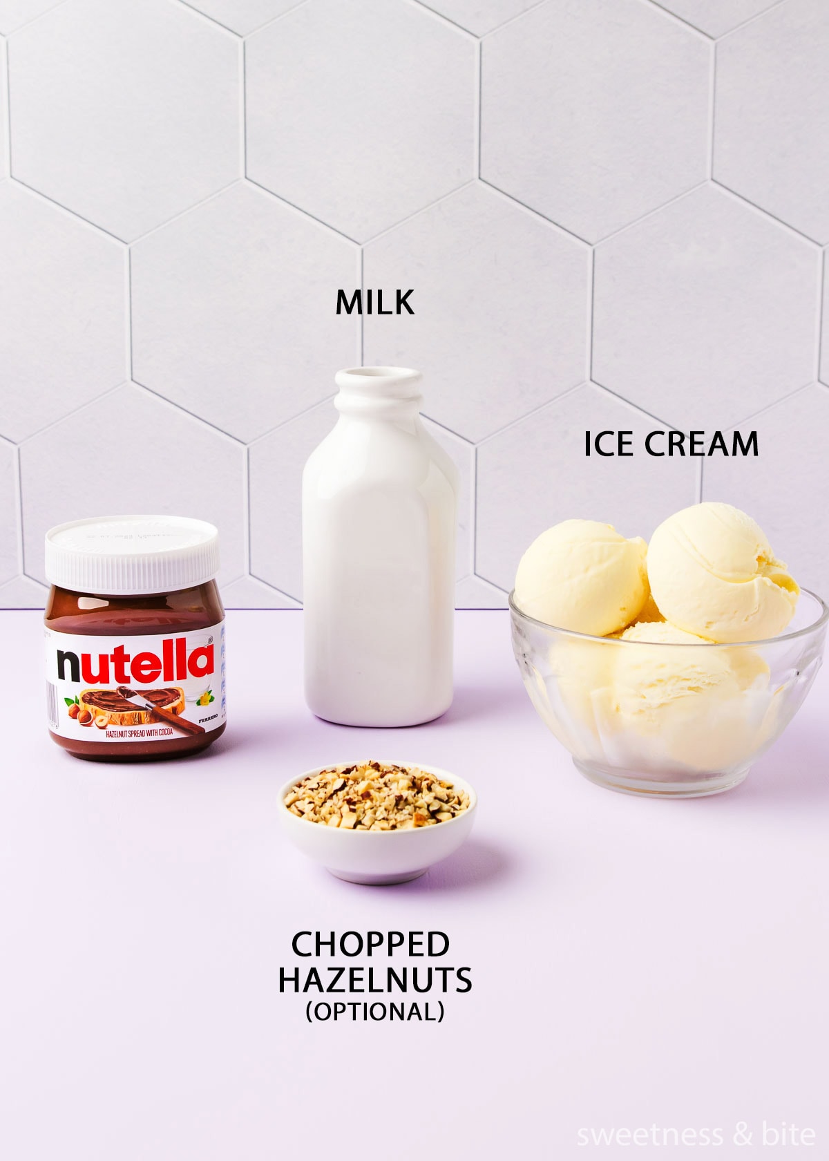 The milkshake ingredients - Nutella, vanilla ice cream, milk and chopped hazelnuts, on a pale purple background. 