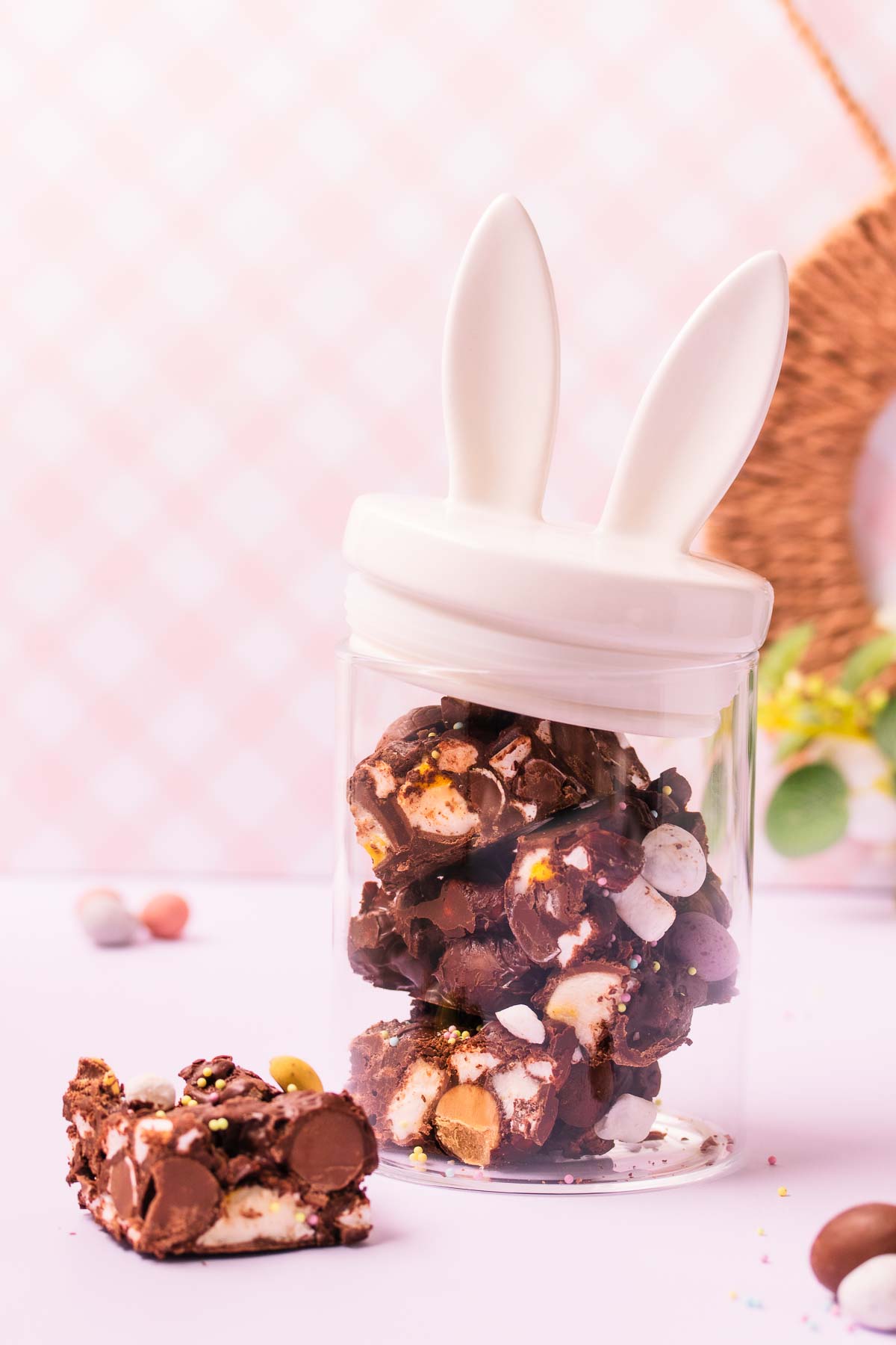 Pieces of Easter egg rocky road in a glass jar that has a white ceramic lid with bunny ears on top.