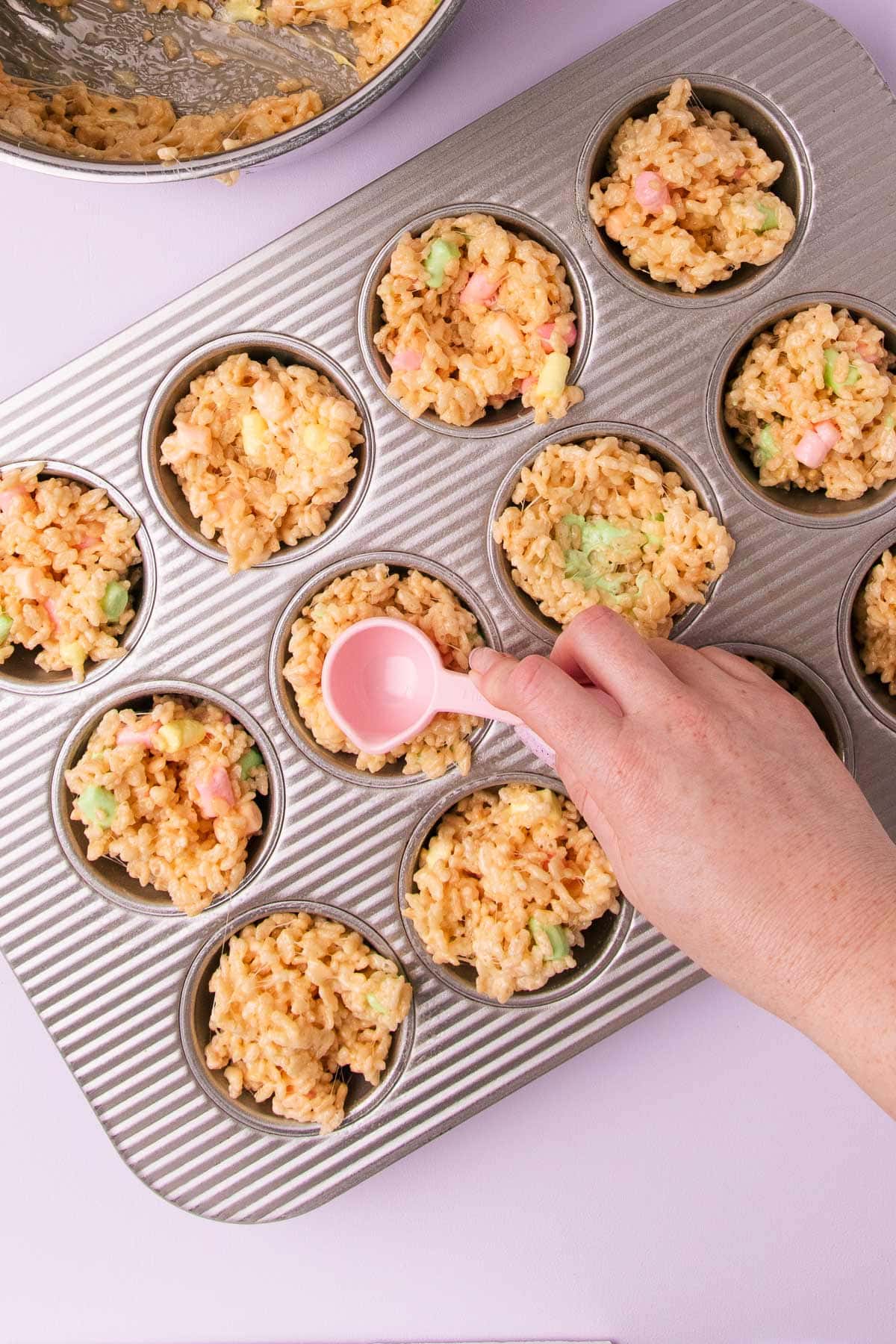A hand using a measuring spoon to press a hole in the middle of the mixture in the muffin pans, to make a nest shape.