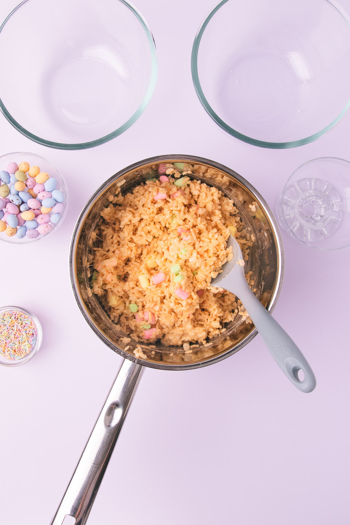 The Easter rice krispie treat mixture in a large stainless steel saucepan on a pastel purple background.