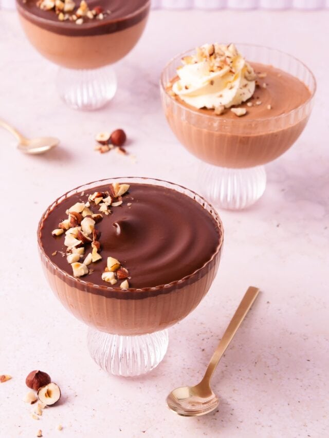 Three scalloped glass footed bowls with Nutella mousse, two are topped with ganache, and one is topped with a swirl of whipped cream.