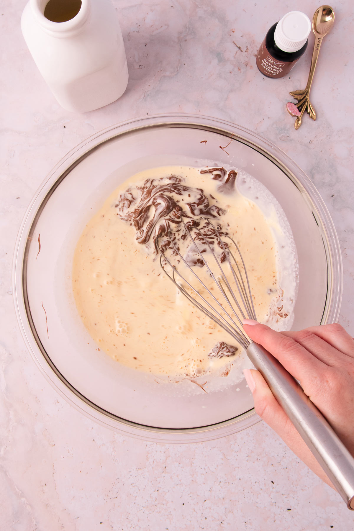 A hand whisking together the hot cream with the melted chocolate and Nutella.