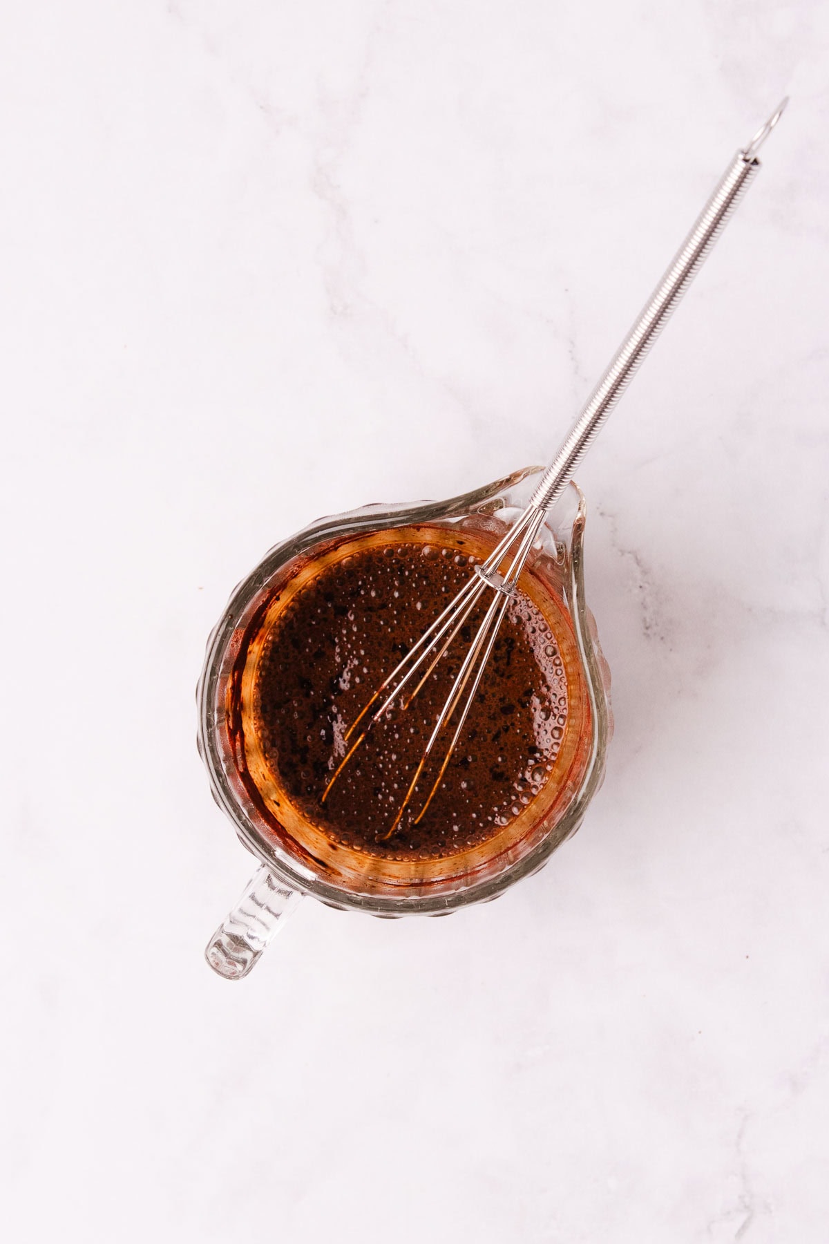 A small glass jug with coffee and cocoa mixed together, with a small metal whisk.
