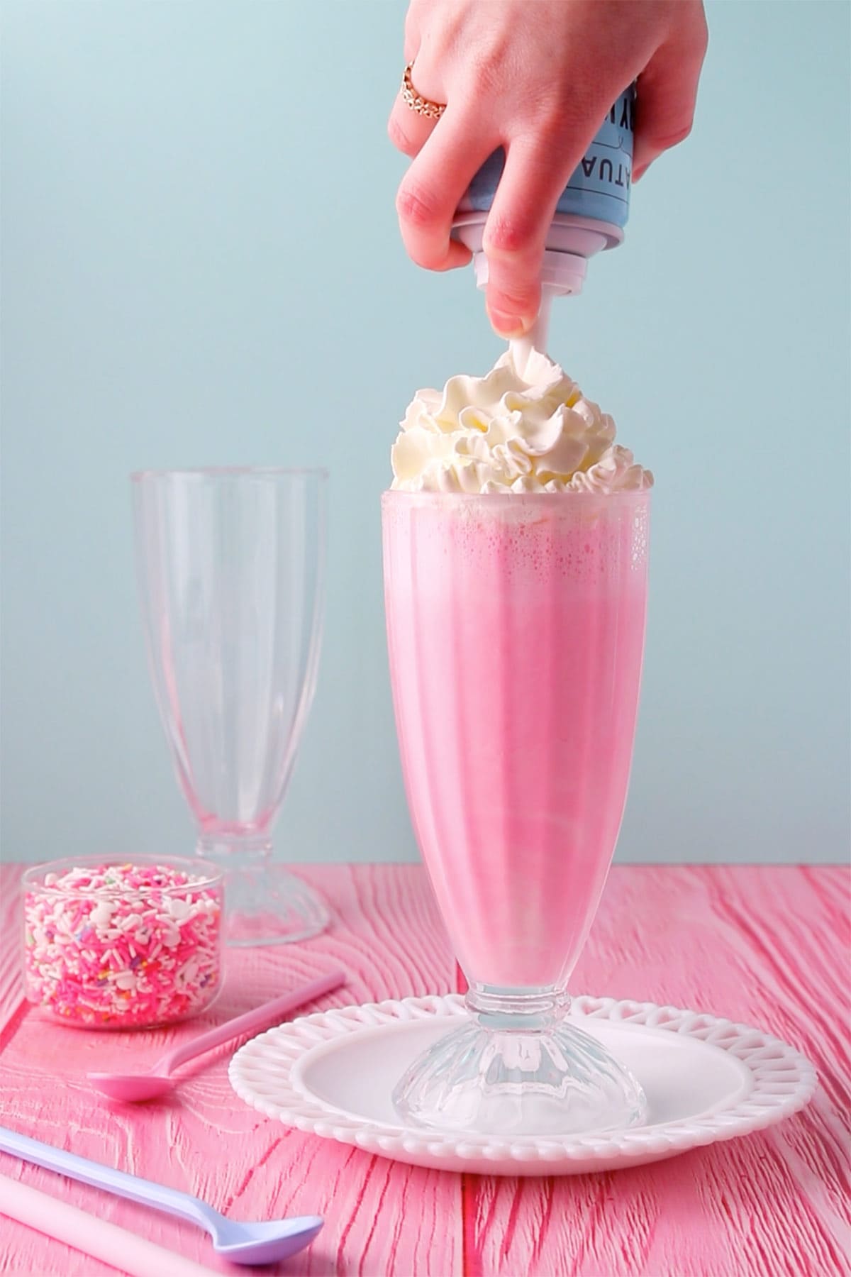 A hand adding whipped cream from a can onto the top of the drink.