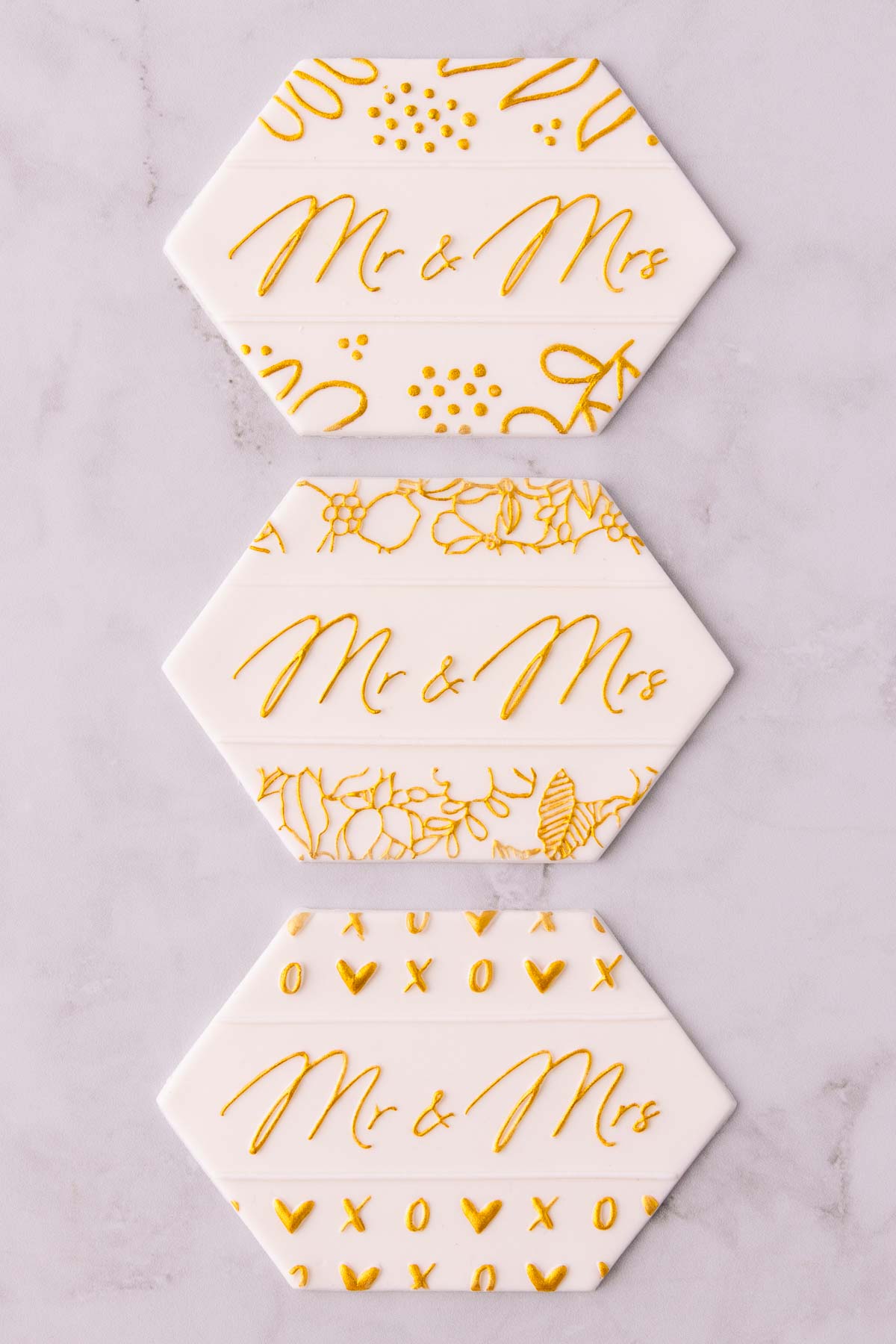 Three stamped fondant designs painted with gold paint, all three say "Mr & Mrs" in the centre, and they have different floral designs around the edges. 