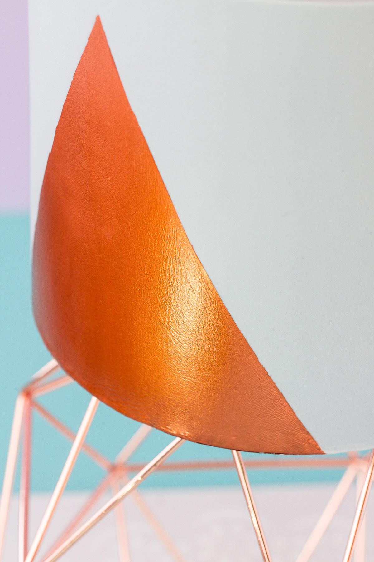 Close up of the bottom edge of a grey fondant covered cake, which has a triangular shape painted on with shiny copper coloured edible paint.