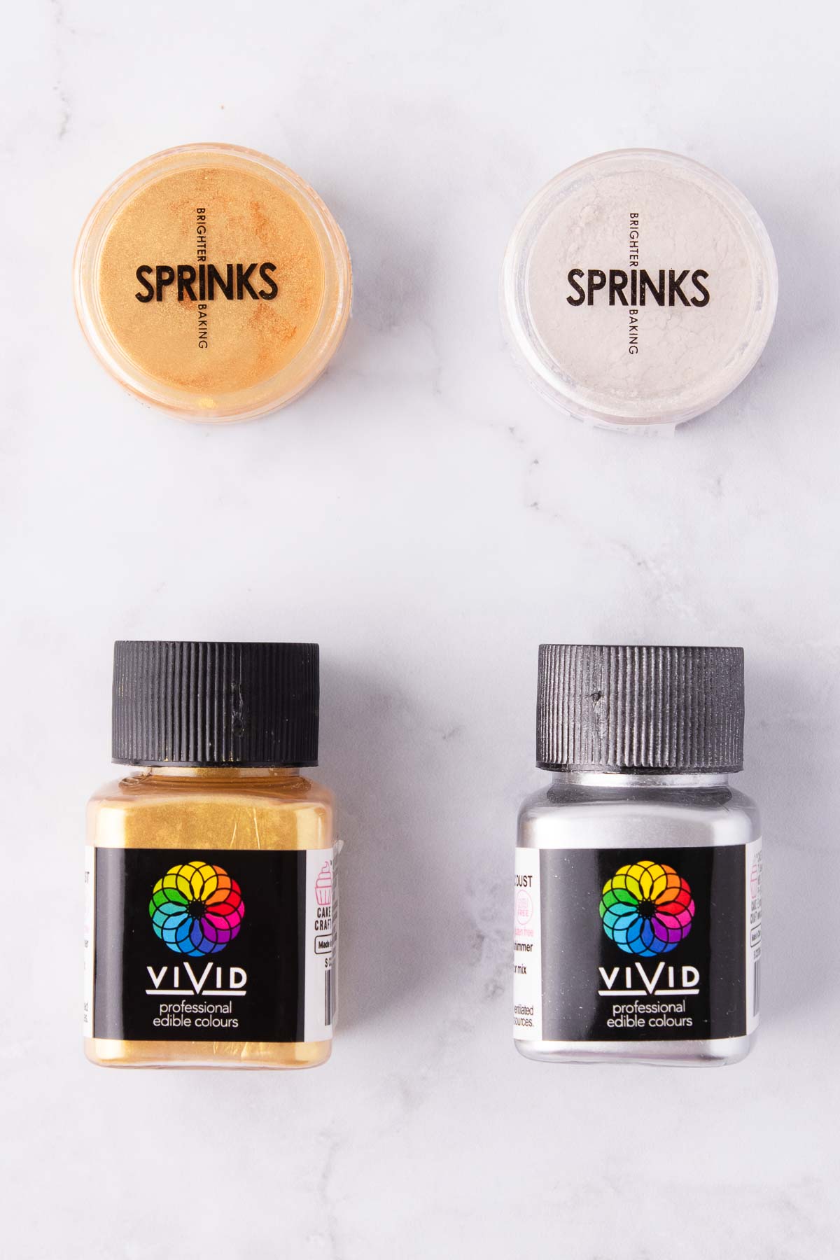 Small containers of edible gold lustre dust on a grey marble background.
