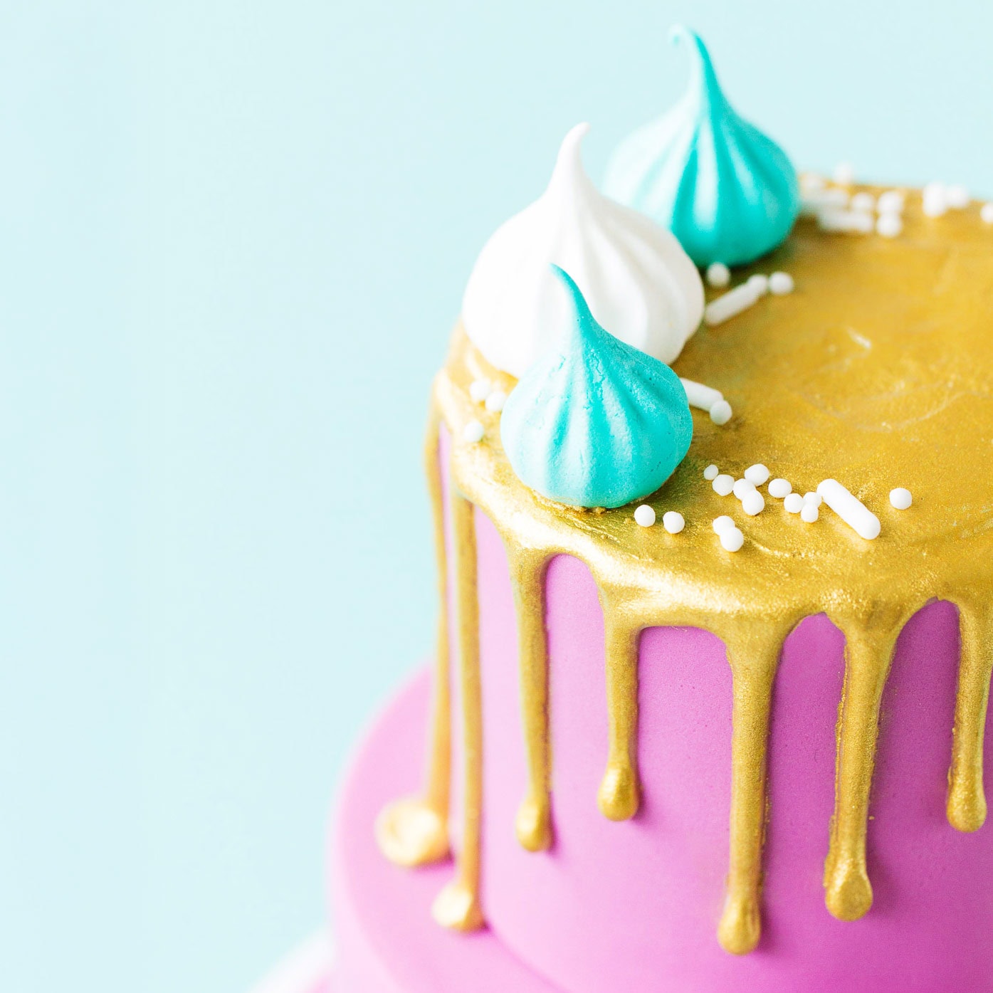 Close up of the top tier of a mini two tier cake covered with purple fondant icing with a metallic gold painted drip on the top tier, and mini meringues.